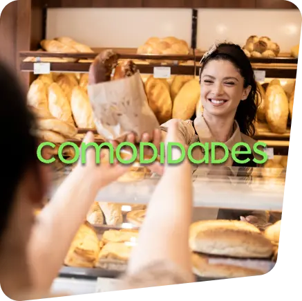 Duas mulheres em uma padaria, sendo uma atendente entregando a sacola de pães para a sua cliente que está do outro lado do balcão.