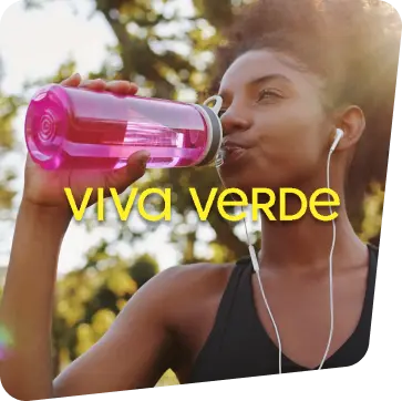 Mulher negra parada em um parque, bebendo água em uma garrafa rosa com fones de ouvido após terminar sua atividade física.